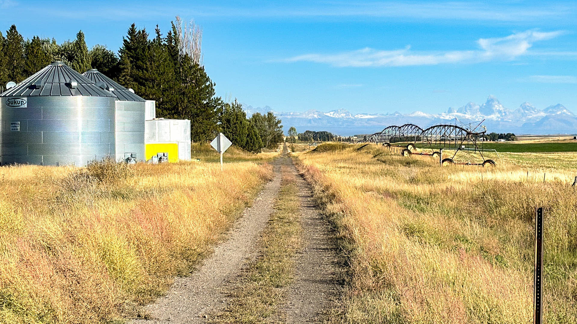 cycling trail in an agricultural field with silos, sprinklers and the Tetons in the background
